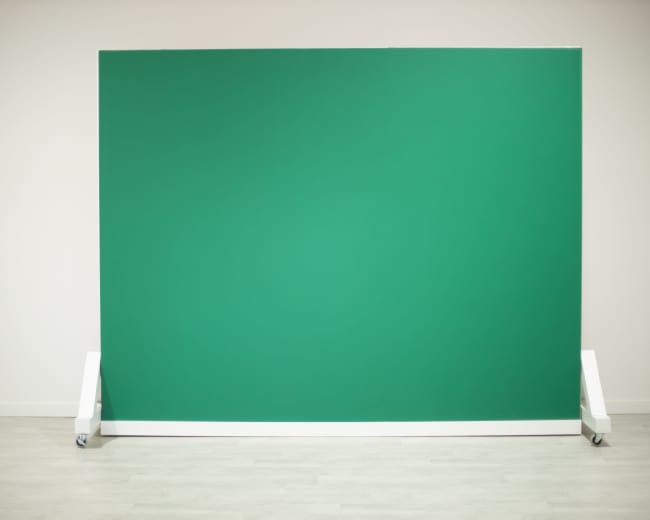 A green backdrop setup on wheels against a plain wall.