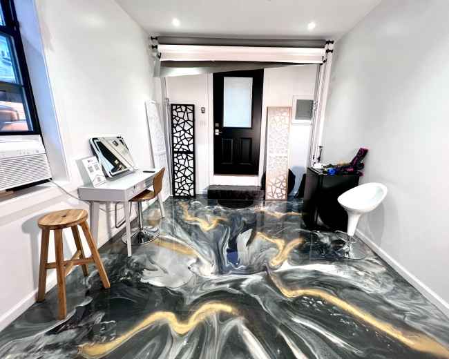 The image shows a modern indoor space featuring a glossy, marbled floor, a small desk with a mirror, a stool, and an entrance with a black door framed by decorative panels.