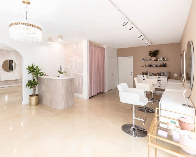 A modern beauty salon interior featuring a reception desk, styling stations, and decorative elements in neutral tones.