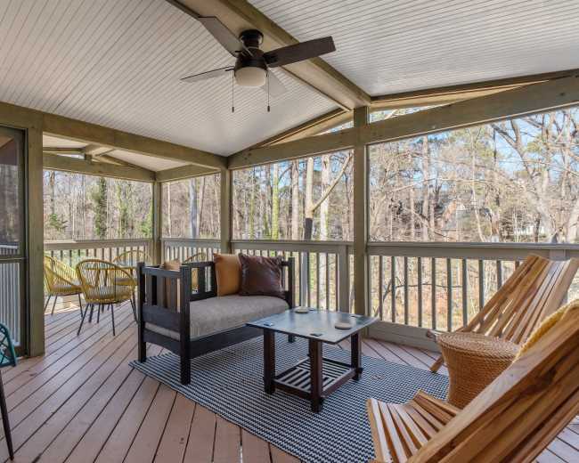 The image shows a screened porch with seating arrangements, including a sofa, coffee table, and various chairs, surrounded by trees.