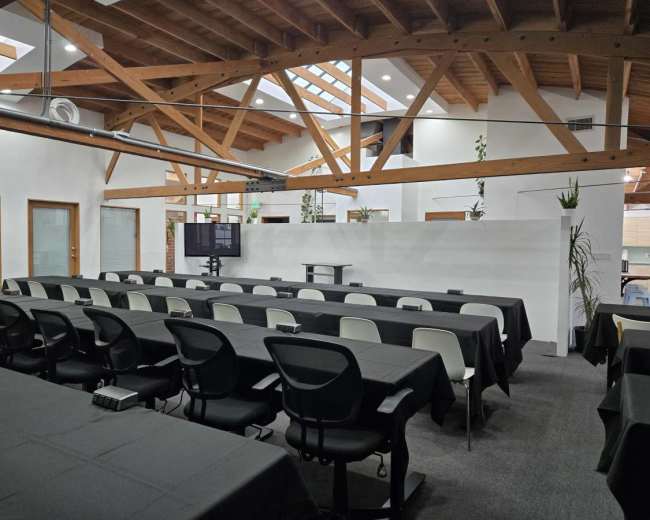 The image shows a spacious conference room with multiple rows of tables covered in black cloth, under a ceiling with exposed wooden beams and skylights.