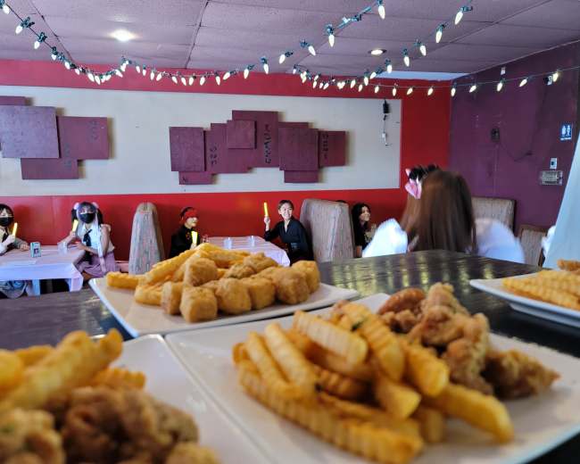 A restaurant interior with tables arranged for dining, featuring plates of fries and chicken in the foreground and patrons in the background.