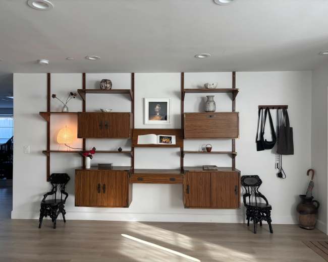 A wooden bookshelf with cabinets and decor items is mounted on a white wall in a well-lit room.