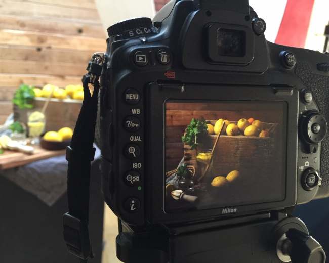 A camera is positioned in front of a rustic setup featuring lemons and a wooden crate on a table.