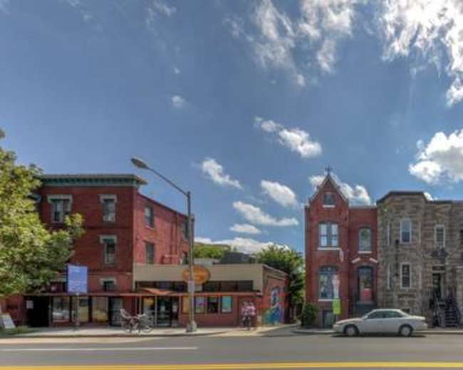 The image shows a row of buildings in varying architectural styles along a city street under a partly cloudy sky.