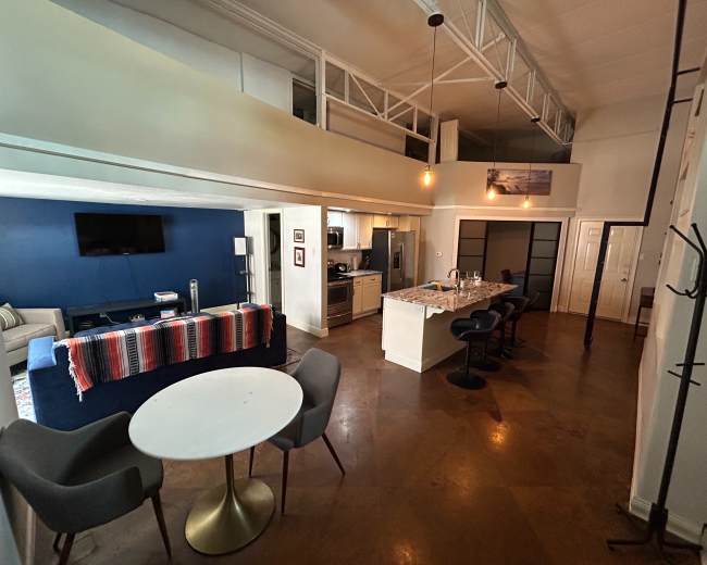 The image shows a modern apartment interior with a kitchen, dining area, and living room, featuring a blue accent wall and open lofted space.