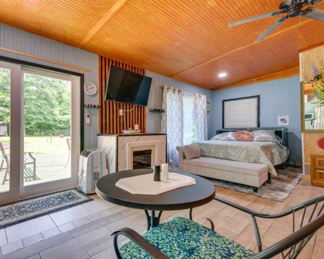 A cozy interior features a seating area, a bed, and a large sliding door leading to an outdoor space surrounded by greenery.