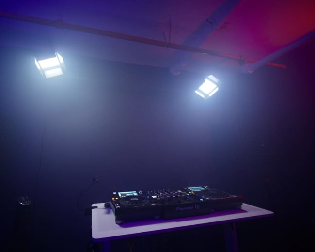 A DJ booth with turntables and lights is set up against a dark wall.