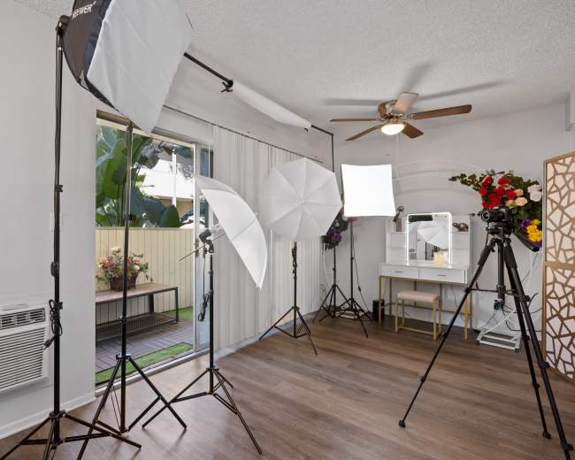 A photography studio setup features multiple softbox lights, tripods, a vanity mirror, and a window overlooking a garden.