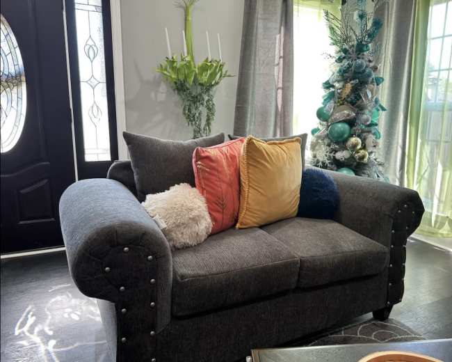 A dark gray couch with colorful pillows sits in a well-lit room featuring a decorative Christmas tree and green curtains.
