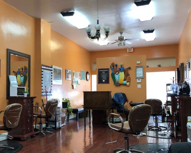 A hair salon interior features orange walls, wooden flooring, and multiple styling stations with salon chairs.