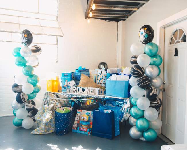 A display of wrapped gifts and balloons in a decorated space for a celebration, with a focus on a table filled with colorful bags and presents.
