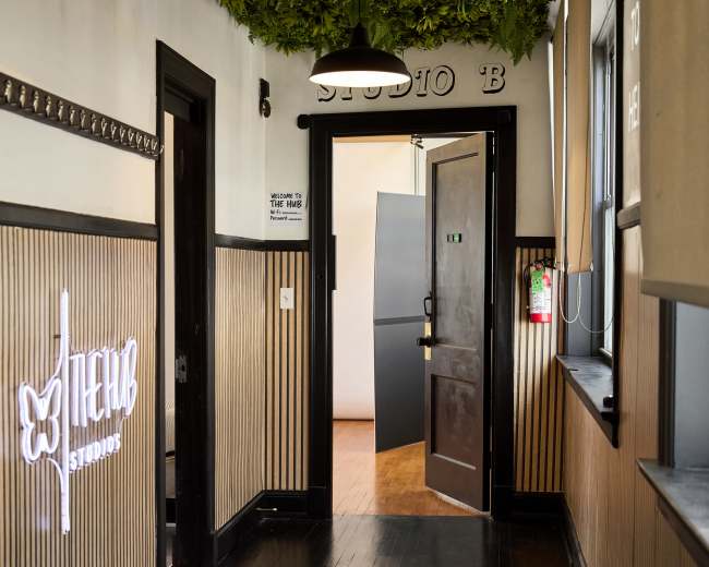 A hallway with dark wooden floors and walls, featuring lush greenery hanging from the ceiling and a door leading to another room at the end.