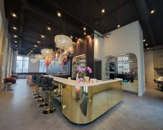The image shows a modern bar area with a gold countertop, several high stools, and elegant chandeliers, complemented by decorative floral arrangements on the walls.