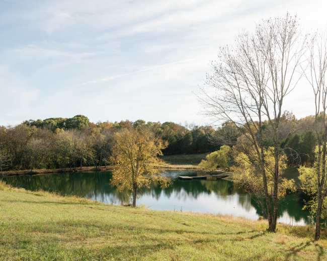 A serene pond reflects the clear sky, surrounded by trees with autumn foliage.