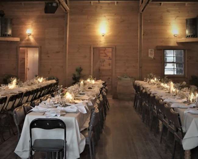 A long hall features neatly arranged tables set for a formal dinner, with candlelight illuminating the wooden interior.