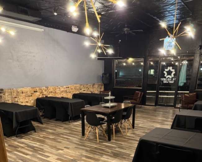 The image shows a spacious restaurant interior with several black tables set up and a decorative lighting feature on the ceiling.