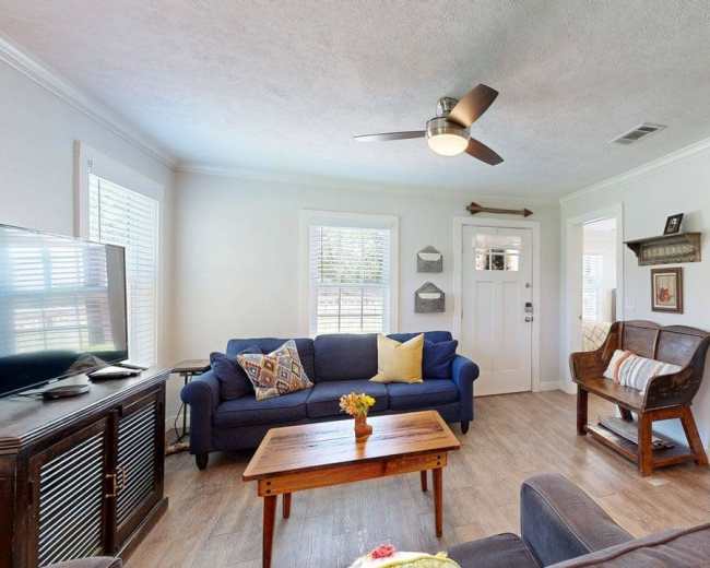 A living room features a blue sofa, a wooden coffee table with flowers, a TV on a cabinet, and a doorway leading to another room.