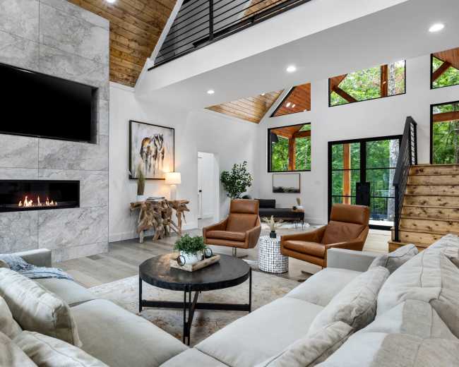 The image shows a modern living room with a marble fireplace, large windows, and contemporary furniture including two leather armchairs and a plush sofa.