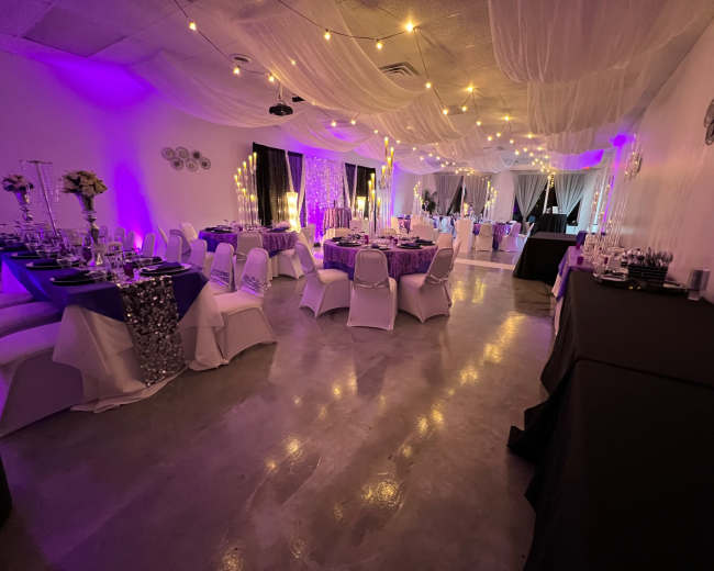 An event space with elegantly set tables, draped fabric, and string lights creating a festive atmosphere.