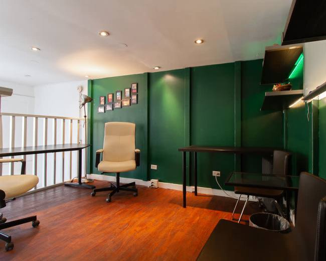 The image shows a small office space with green walls, wooden flooring, a desk, an office chair, and a wall displaying several framed photographs.
