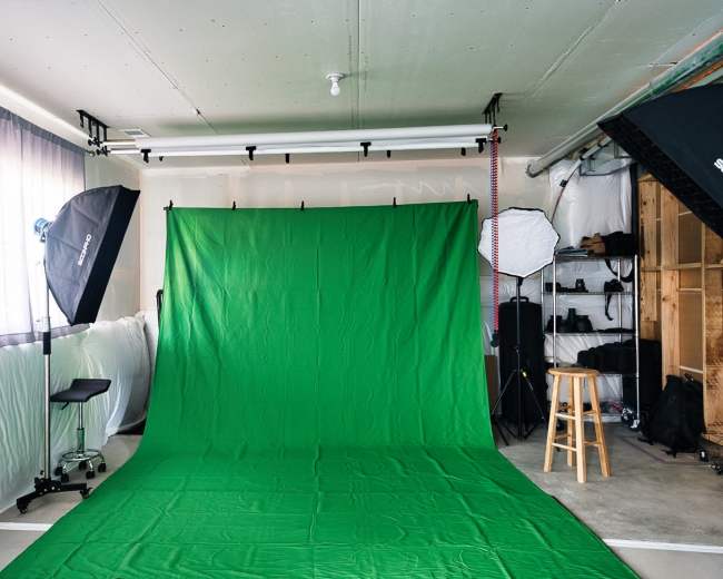 A green backdrop is set up in a well-lit studio space with various lighting equipment and a stool.