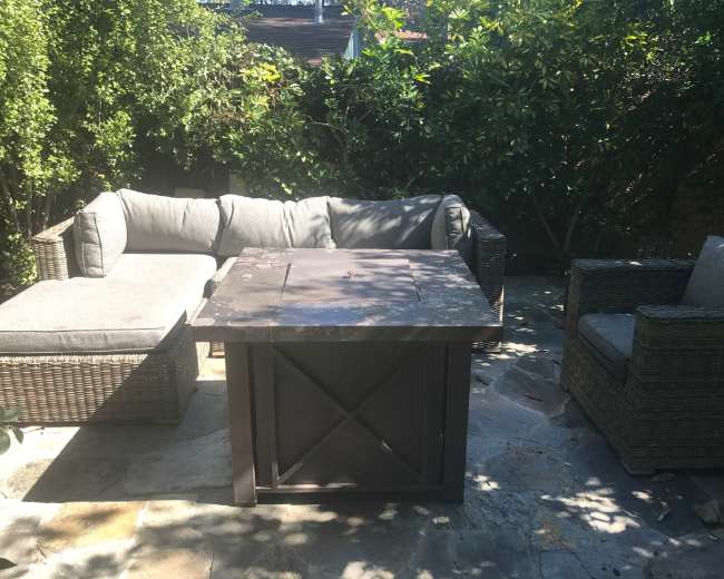 A patio area features a sectional sofa and two armchairs surrounding a square table, with greenery in the background.