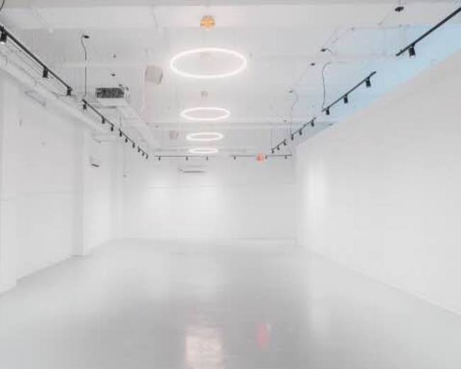 The image shows a spacious, minimalist white room with circular ceiling lights and a polished floor.