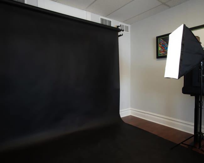 A photography studio setup featuring a black backdrop and a softbox light on a stand.