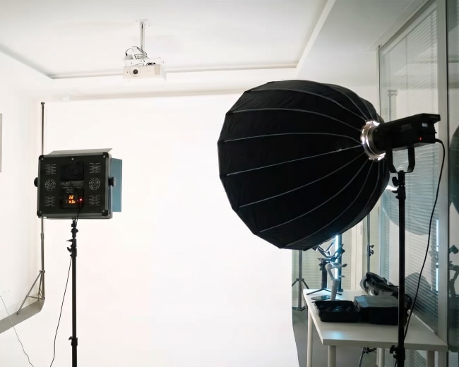 The image shows a photo studio setup with two large softbox lights positioned on either side of a blank backdrop.