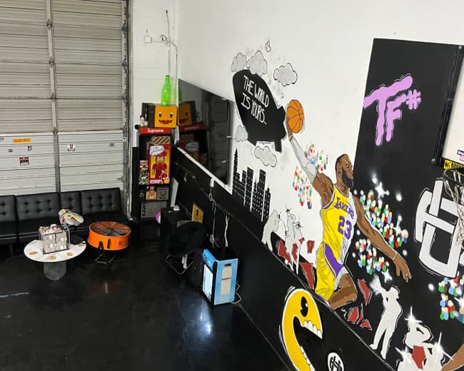 The image shows an urban-themed room with a mural of a basketball player on the wall, various gaming machines, and seating areas.