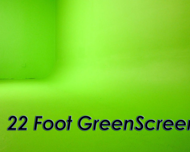 The image shows a bright green studio space featuring a 22-foot green screen seamlessly extending from the floor to the wall.