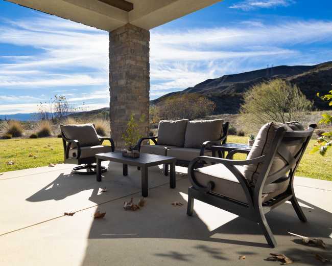 A patio area features a table and four chairs with a view of mountains and blue skies in the background.