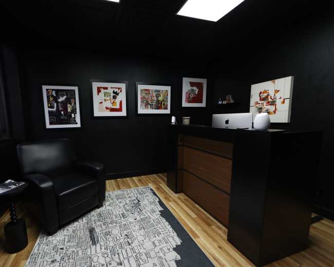 The image shows a modern office space featuring a black leather chair, a wooden reception desk, and framed artwork on the walls.