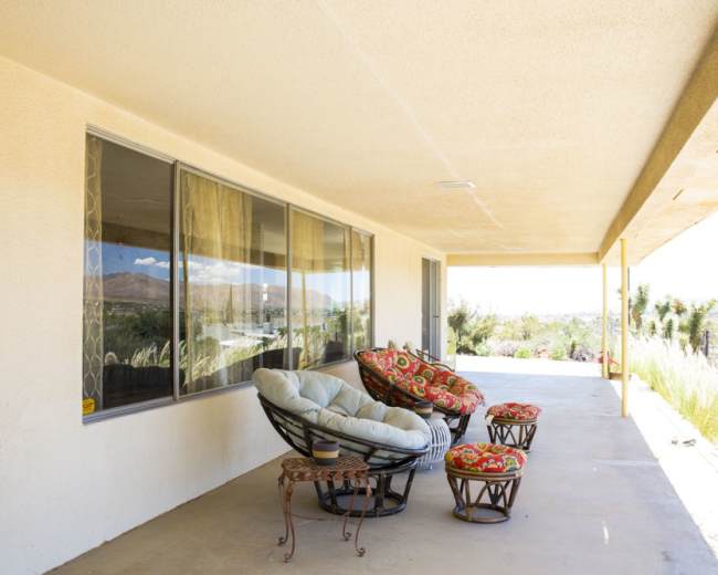 A covered porch features a set of patterned upholstered chairs and a small round table overlooking a landscape.