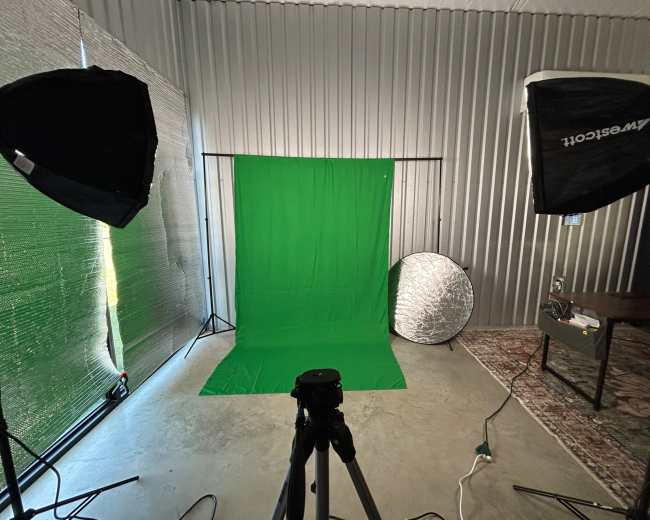 The image shows a photography setup with a green backdrop, two softbox lights, a tripod, and a reflector, all arranged in a studio space.