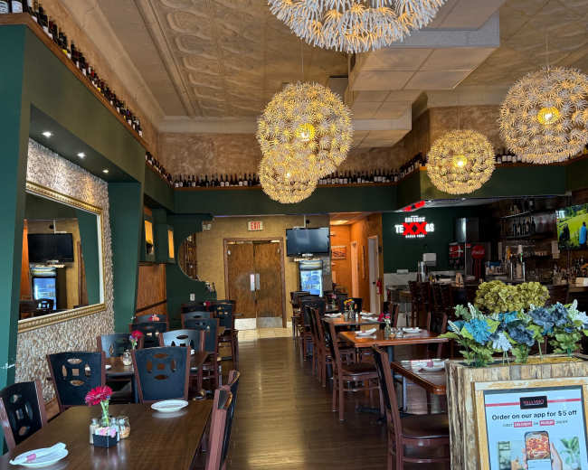 The image shows a spacious restaurant interior with wooden tables, chairs, and decorative lighting fixtures hanging from the ceiling.