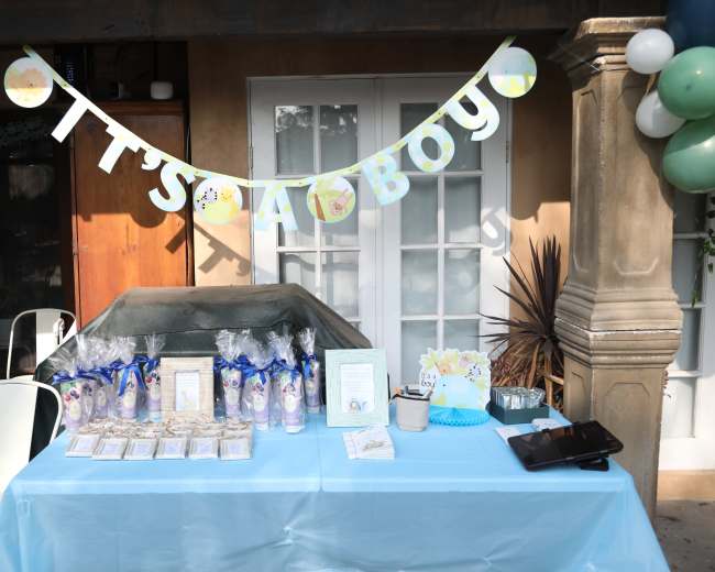 A decorated table showcases party favors and treats with a banner reading "It's a Boy" in a festive setting.
