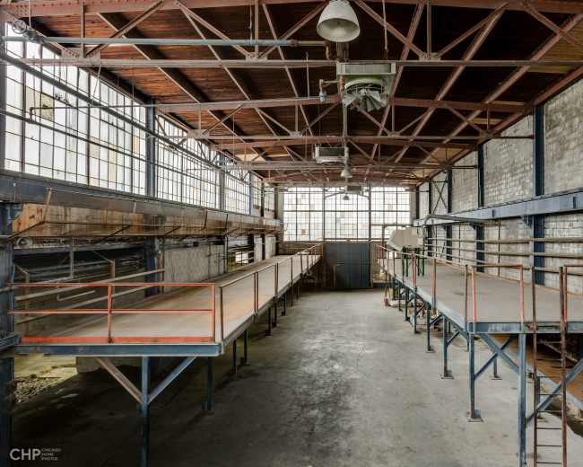 An empty industrial warehouse with high ceilings, large windows, and elevated platforms along the walls.