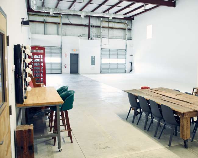 The image shows a spacious, industrial-style room with a long wooden table, chairs, and a vintage telephone booth in the background.