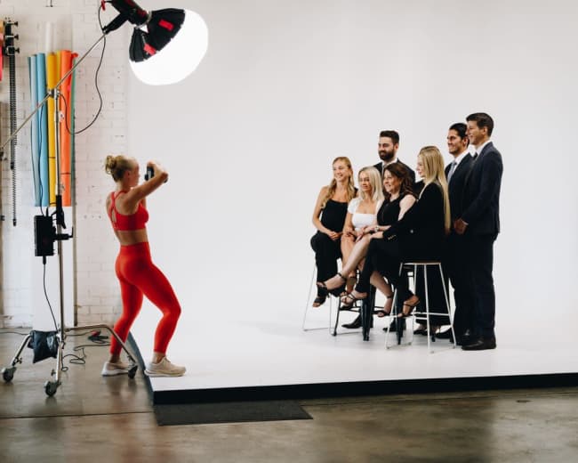 A photographer captures a group of seven people posing on a white backdrop in a studio setting.