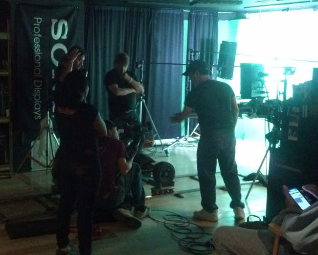 A film crew is setting up equipment and adjusting cameras in a studio environment for a production.