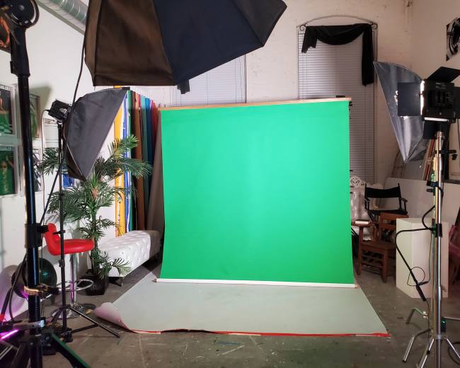 A photography studio setup with a green backdrop, lighting equipment, and various accessories arranged around the space.