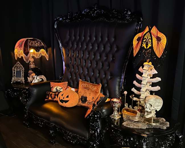 A vintage black loveseat is adorned with Halloween decorative items and set against a dark background.