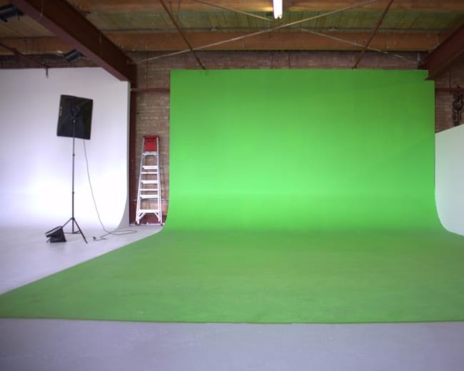 A green screen setup in a studio with a ladder and a floor covered in gray paint.