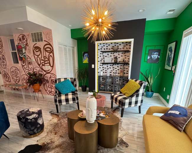 The living room features a mix of colorful furniture including patterned chairs, a yellow sofa, and a coffee table, with artistic wall designs and a bright green accent wall.