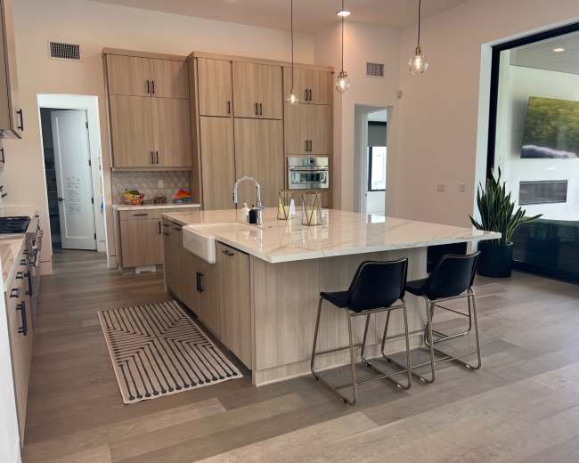 A modern kitchen featuring light wood cabinetry, a large island with seating, and minimal decor.