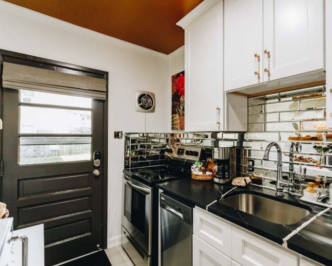 The kitchen features white cabinetry, mirrored backsplash, stainless steel appliances, and a dark countertop, with a door leading outside.