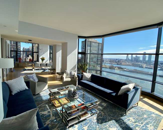 A modern living room with large windows offering a view of a city skyline and water.