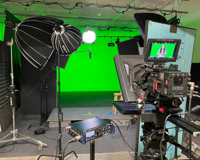 A television studio setup features lighting equipment and a green screen backdrop.